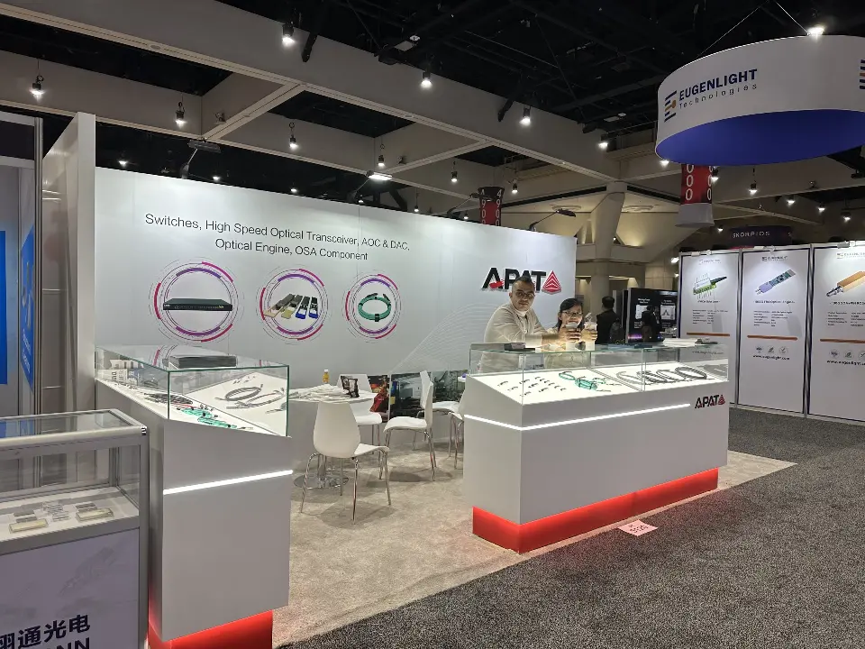 APAT booth with white logo wall, red-lit showcases and lounge seating at the side