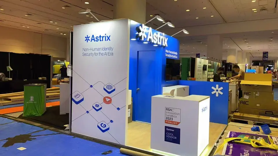 Side view of the Astrix stand showing the white graphic wall with blue icons and lit counter