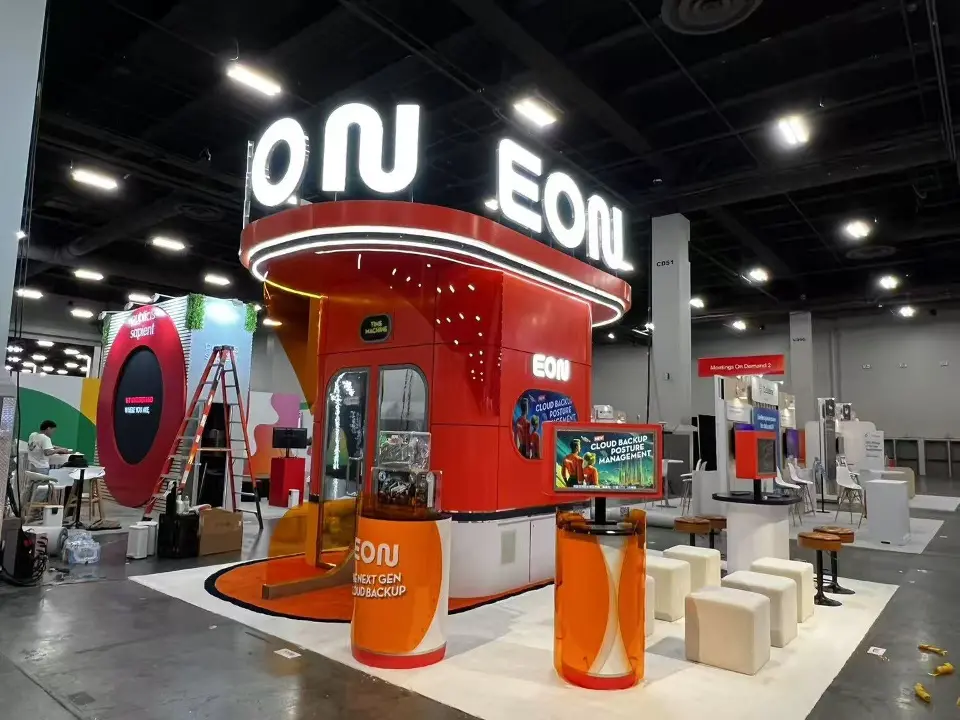 Wide view of the orange EON tower with lit letters, kiosks and white high stools