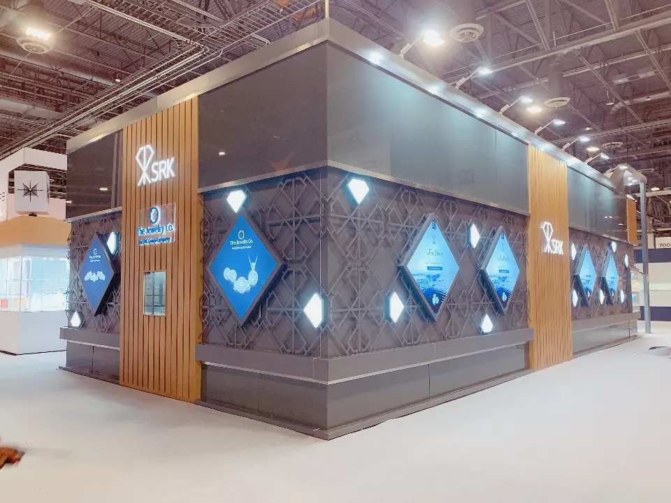 Corner of the SRK booth with wood-look pillars, lit logos and diamond-shaped graphics