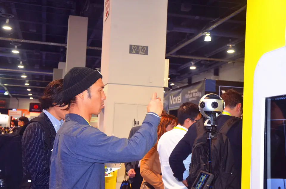 Visitor trying a 360 camera rig among a crowd at the yellow booth