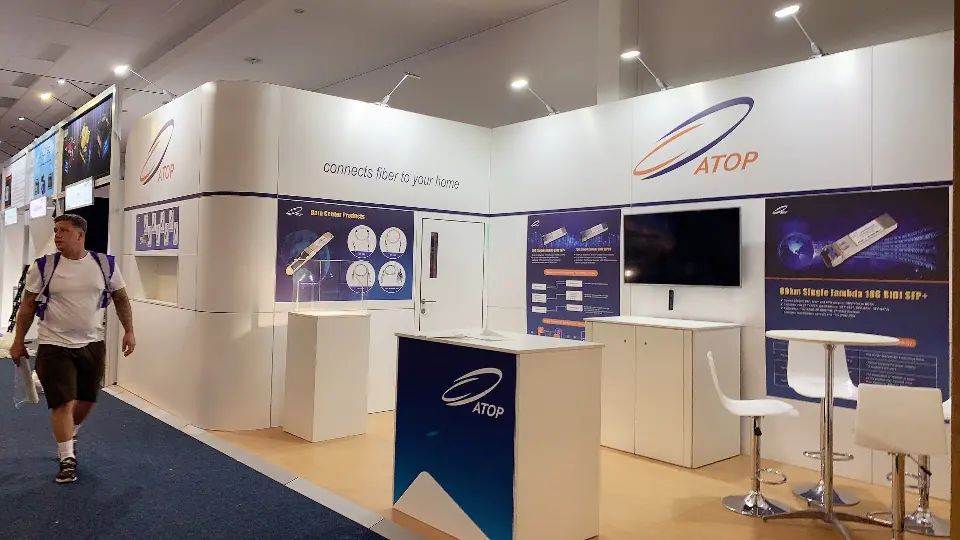 Wide view of the ATOP booth with curved white walls, navy graphics and white bar tables