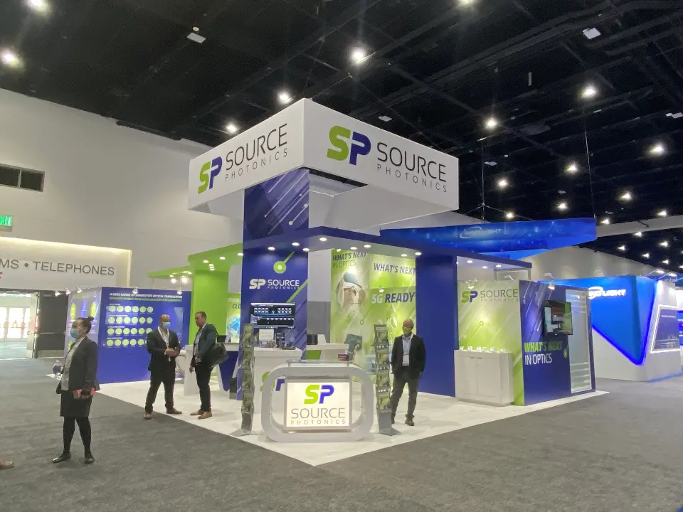 Front of Source Photonics booth with SP Source header, lit counter and green panels
