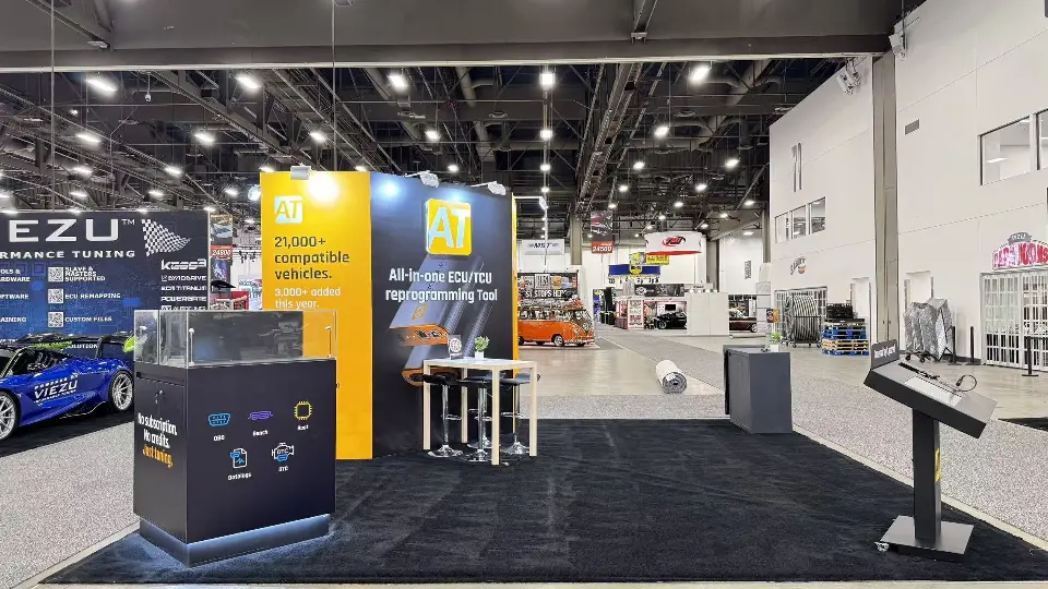 Open booth with yellow and blue graphic walls, a dark kiosk counter and touchscreen stand