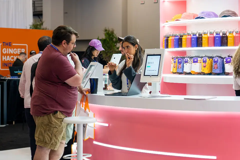 Visitors checking in at an AIR tablet kiosk beside shelves of water bottles and socks