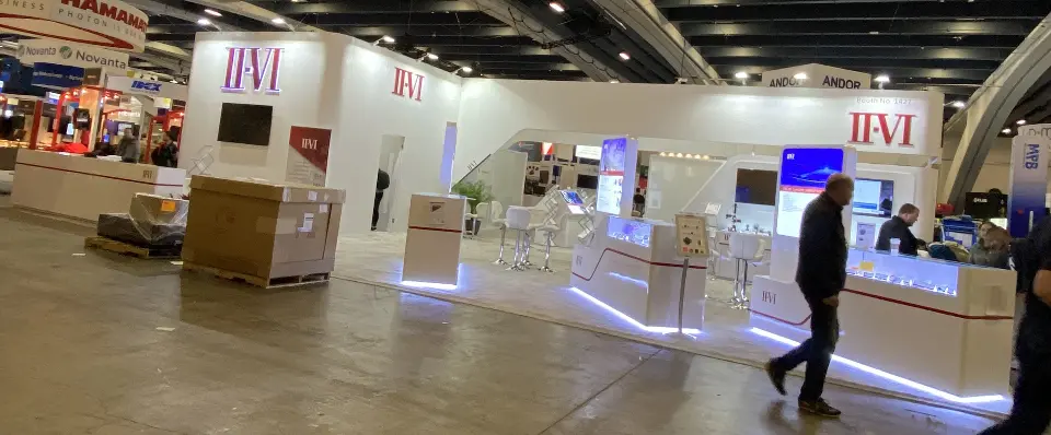 Panoramic front view of the white II-VI booth with lit counters and screens