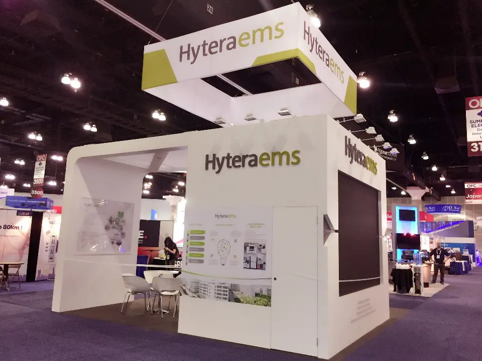 Corner view of the white Hyteraems booth with product panels, meeting table and screen
