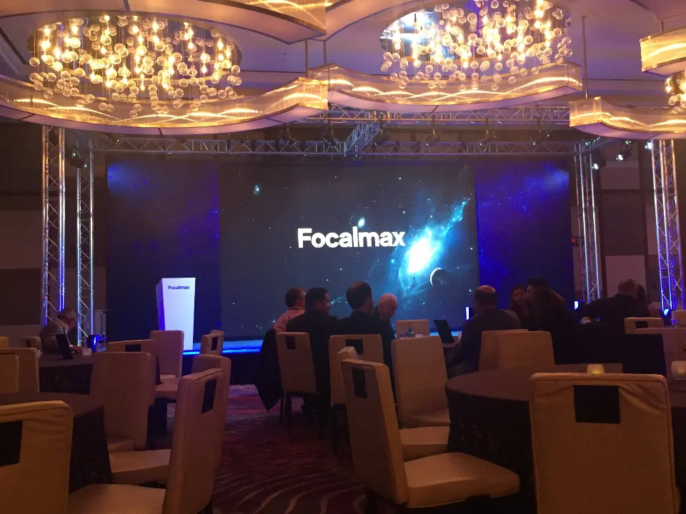 Ballroom view of tables, chandeliers and the Focalmax logo on stage