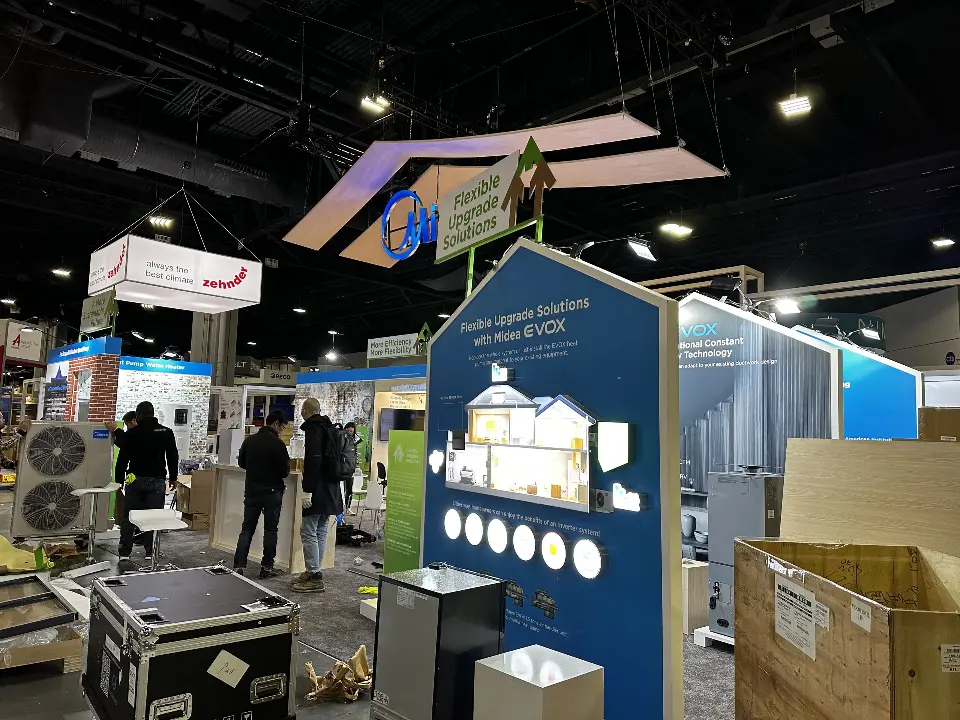 Blue house-shaped Midea display panel with circular product icons and crates nearby
