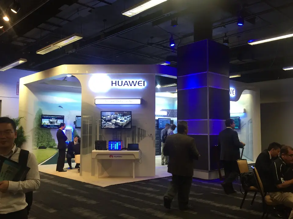 Huawei booth under blue lighting with visitors and screens along the back wall