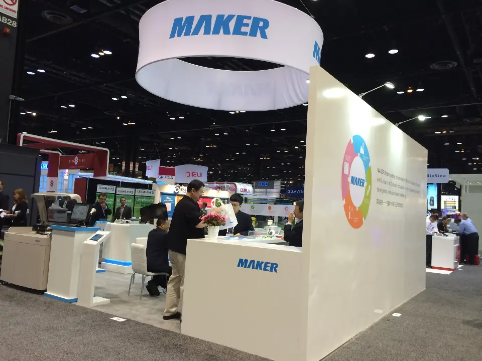 White MAKER booth with round hanging sign, curved counter and analyzer display