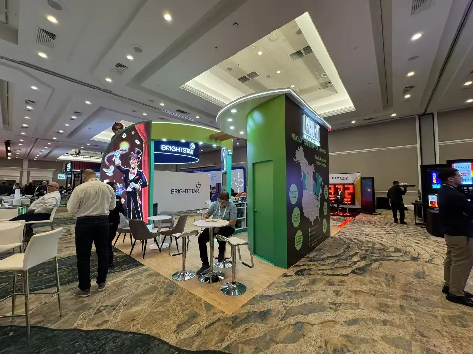 Back corner of the booth with a dark map tower, a green wall and guests at white tables