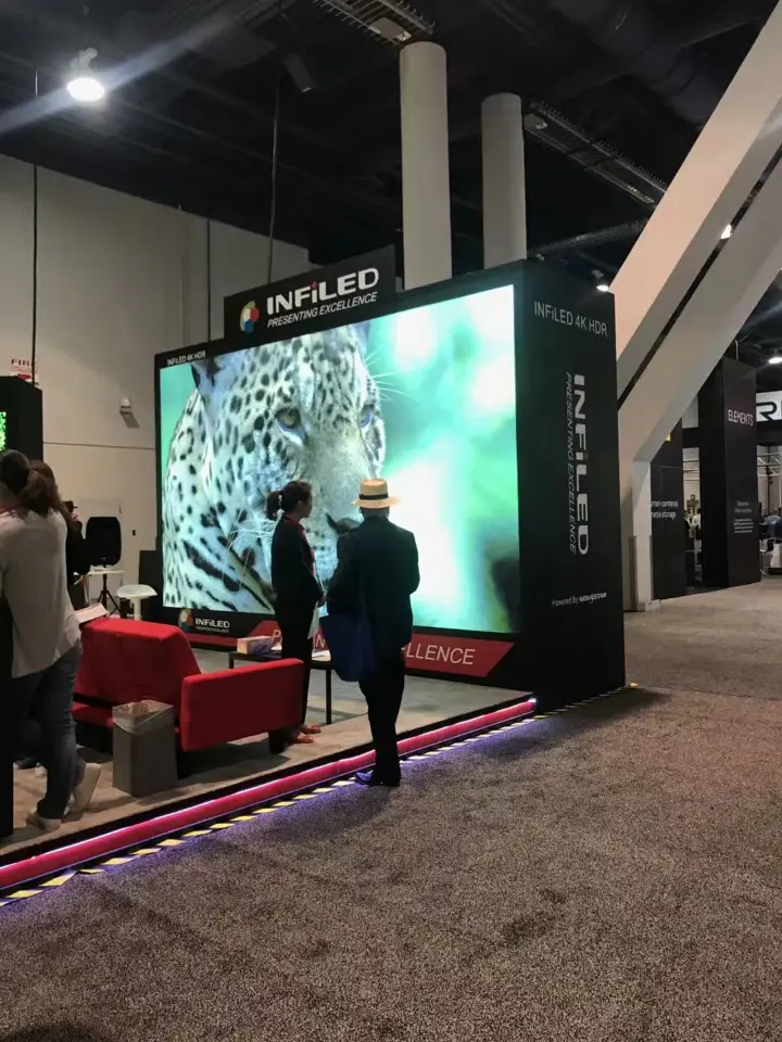 Visitors passing a large screen showing a wildlife scene beside the booth