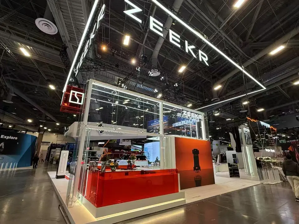 Glass-walled room with red counter wall and screens inside the ZEEKR booth