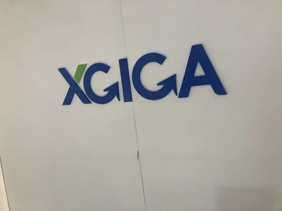 Blue dimensional XGIGA logo on a white wall