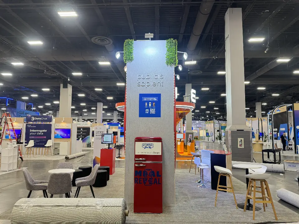 Side of the booth with tall branded column, red kiosk and lounge chairs