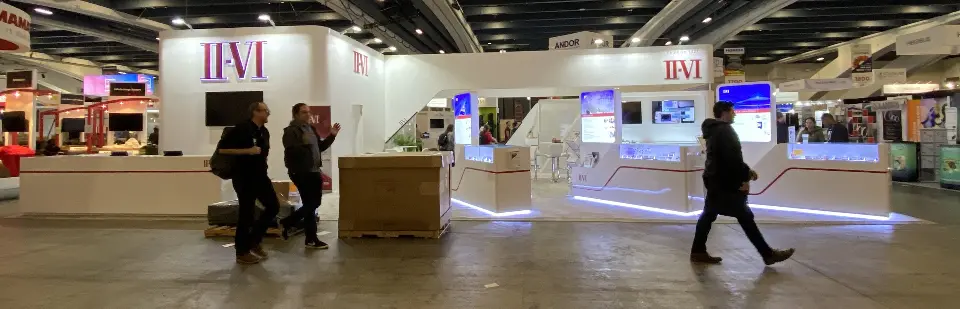 Wide panorama of the booth frontage with visitors passing the white walls