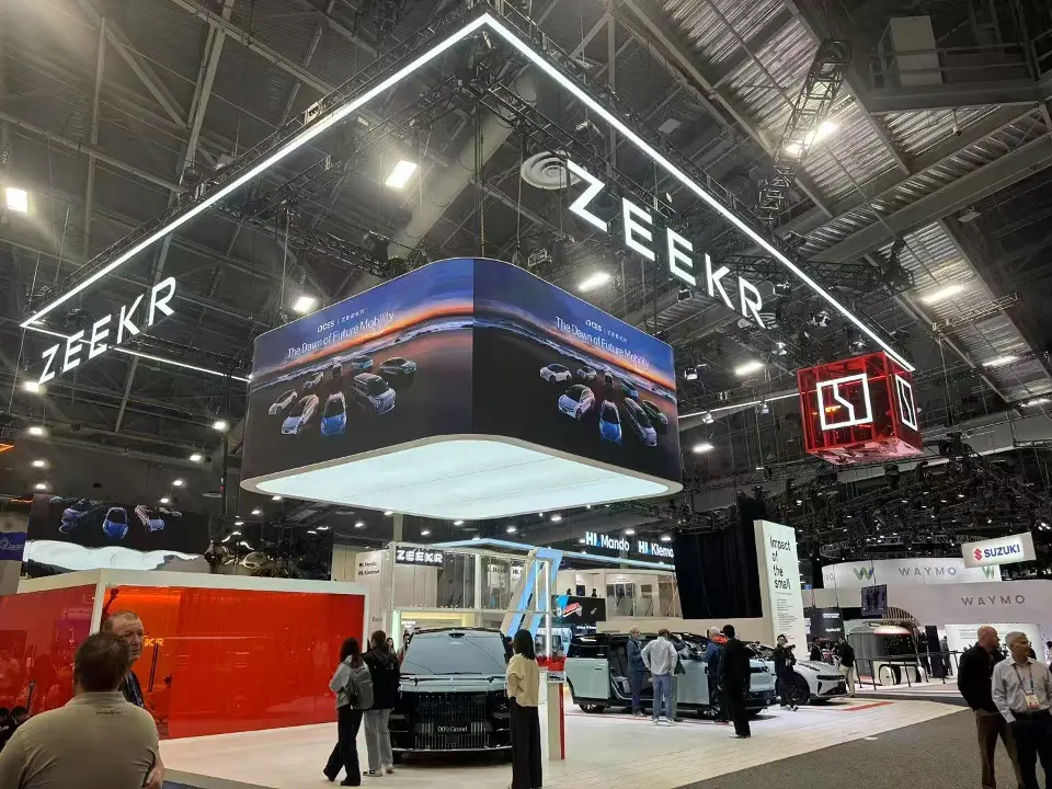 Large curved screen ring over the booth showing vehicle imagery above a red counter wall
