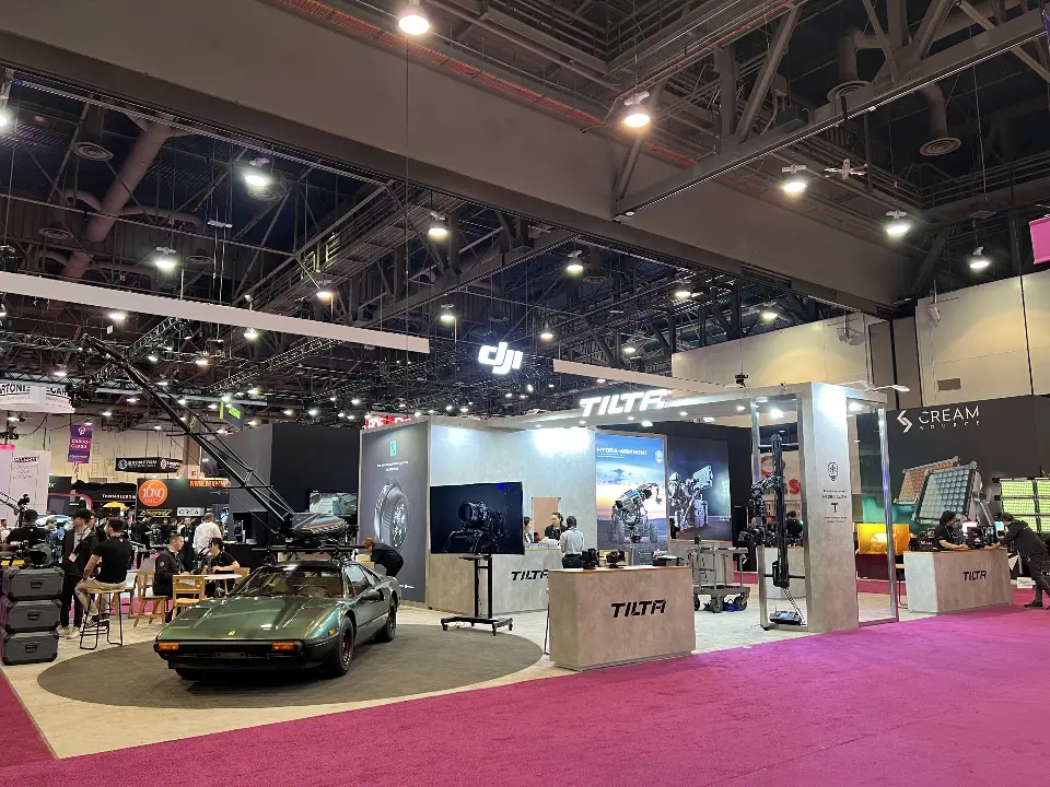 Tilta booth with vintage car on round carpet, camera crane, stone-look counters and lit Tilta header