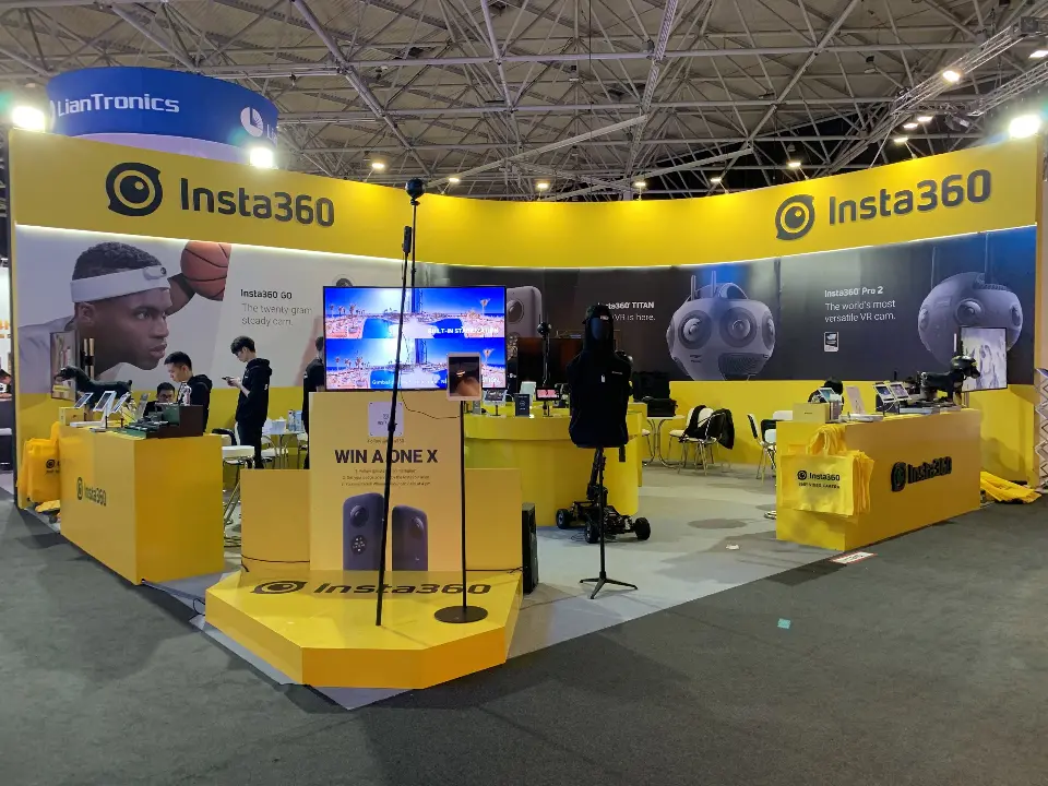 Front view of the yellow Insta360 booth with curved fascia, podium and screen