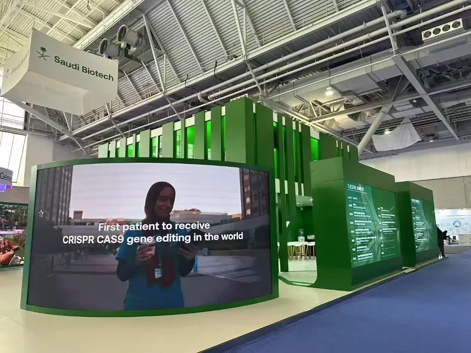 Curved video screen showing a patient story beside green fins and hanging sign