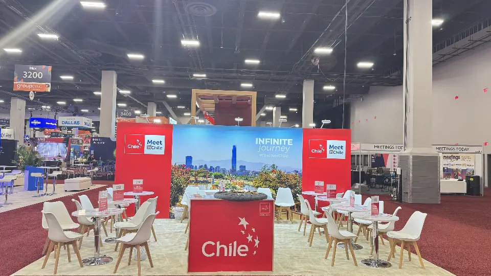 Straight-on view of the Chile Pavilion with skyline backwall, red Chile counter and white meeting chairs