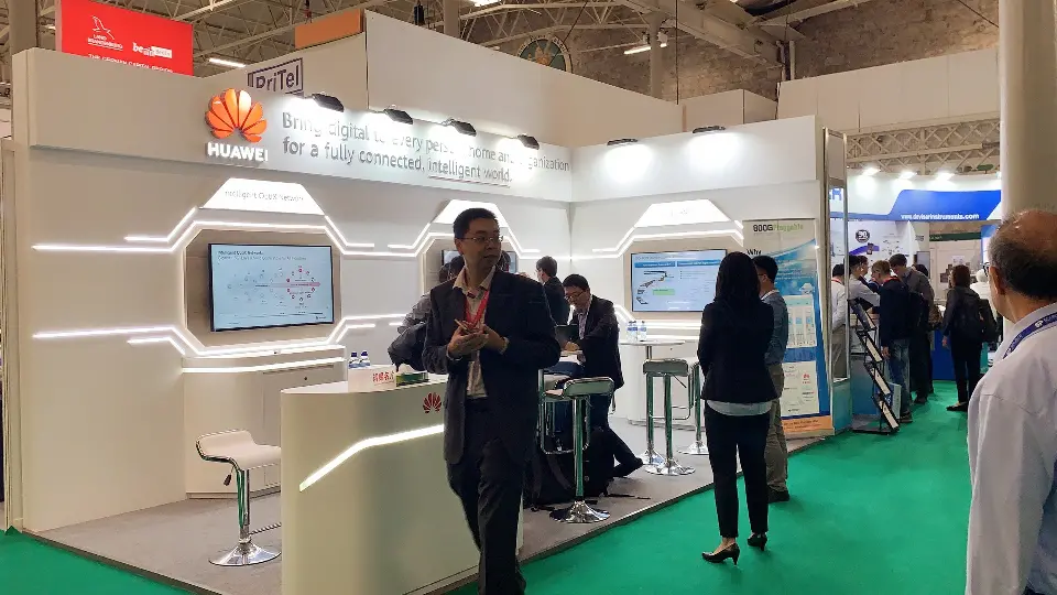 Finished HUAWEI booth on green carpet with a visitor at the counter and light lines across the wall