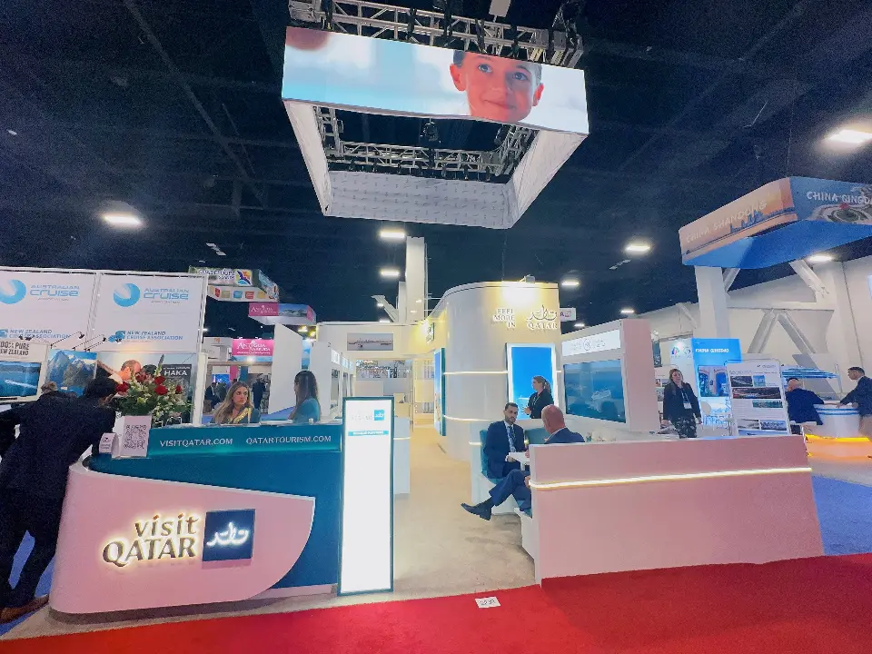 Pink Visit Qatar counter with staff and the hanging sign above