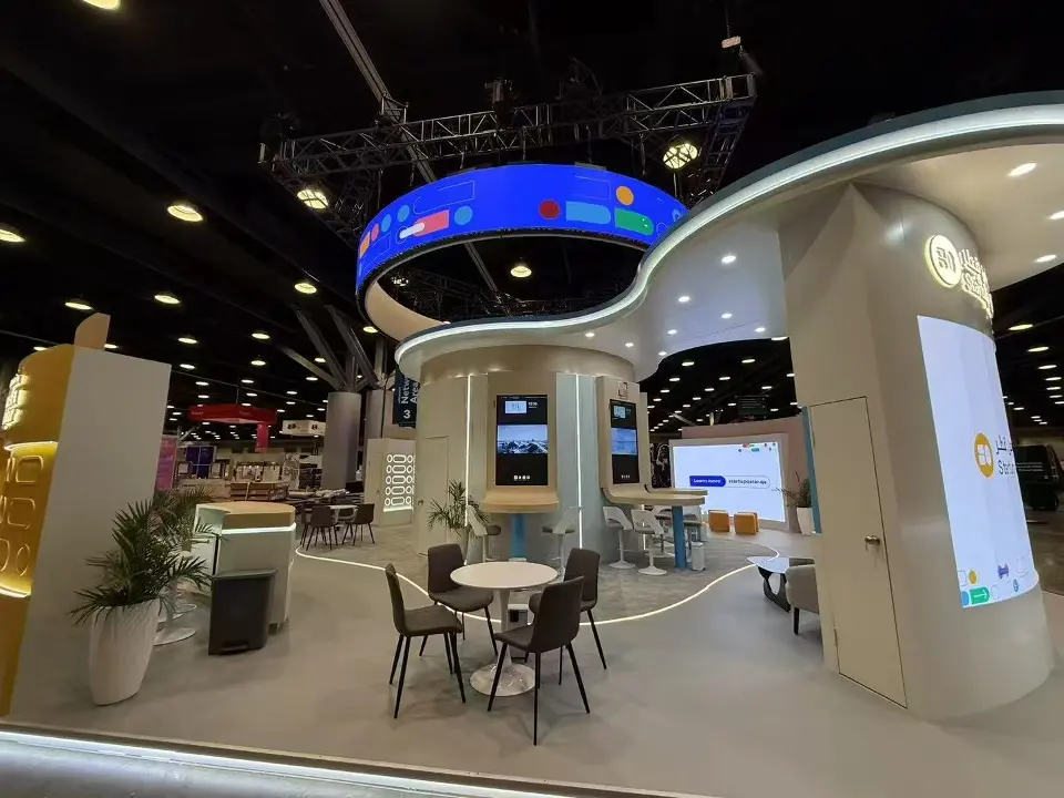 Startup Qatar booth with curved beige walls, a lit blue ring overhead and cafe tables