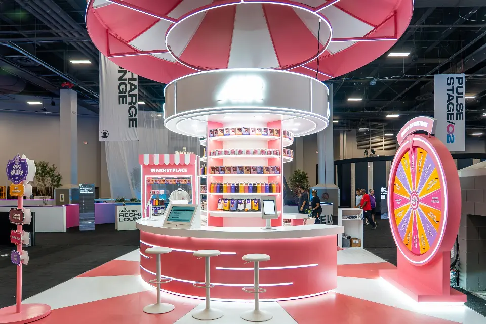 Pink AIR counter with white bar stools, a lit spin-the-wheel stand and the Marketplace kiosk behind