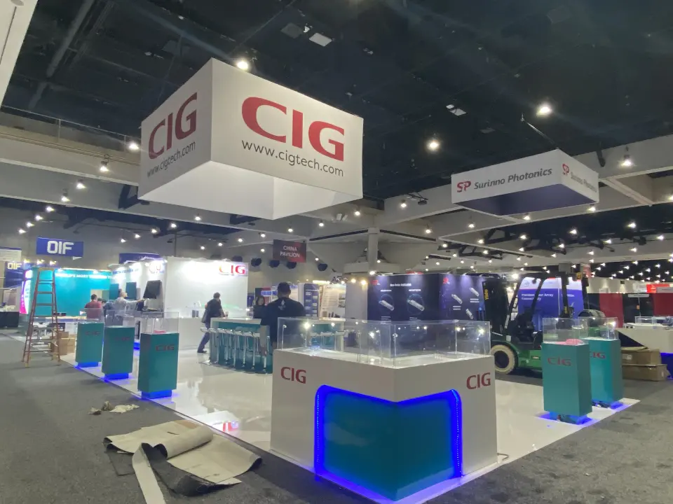 CIG island at OFC with red-logo hanging header and teal glass-top plinths