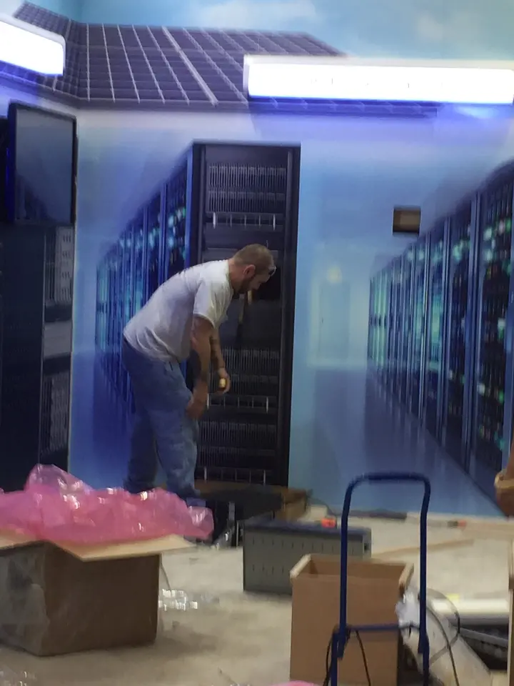 During installation: worker setting up server cabinets in front of the sky mural