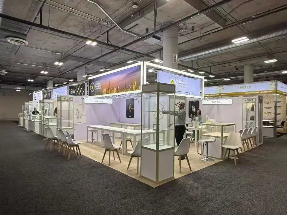 White pavilion booth with lit header graphic, glass showcases and white tables and chairs