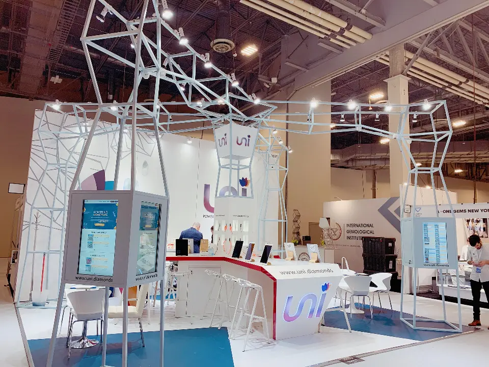 Visitor at the uni booth beside kiosks and the white logo back wall