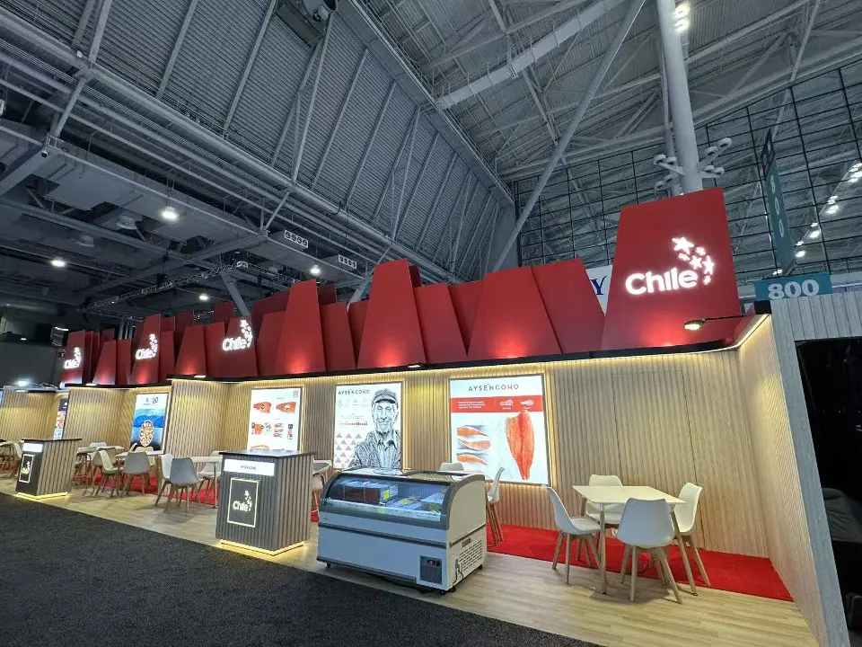 Long view of the Chile booth with red sawtooth header, meeting tables and display fridge
