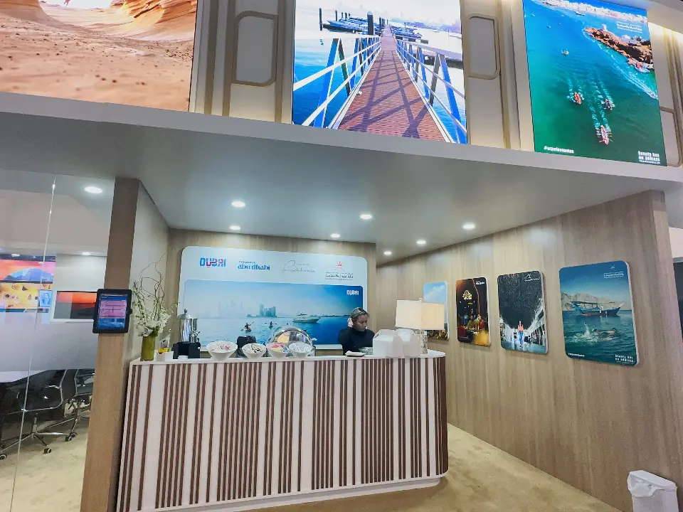 Reception desk with striped front, Dubai graphics and framed coastal photos inside the booth