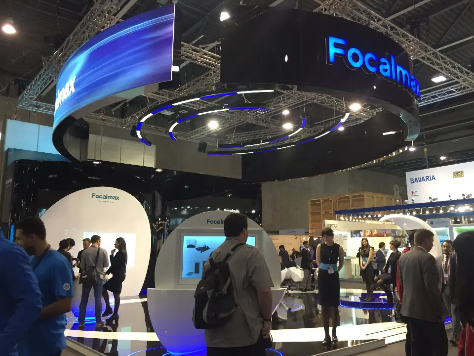 Visitors gathered under the Focalmax ring header near a screen kiosk