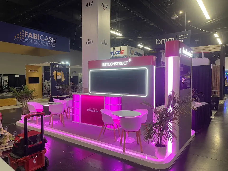 Corner view of the BetConstruct booth with magenta light strips and palm plants