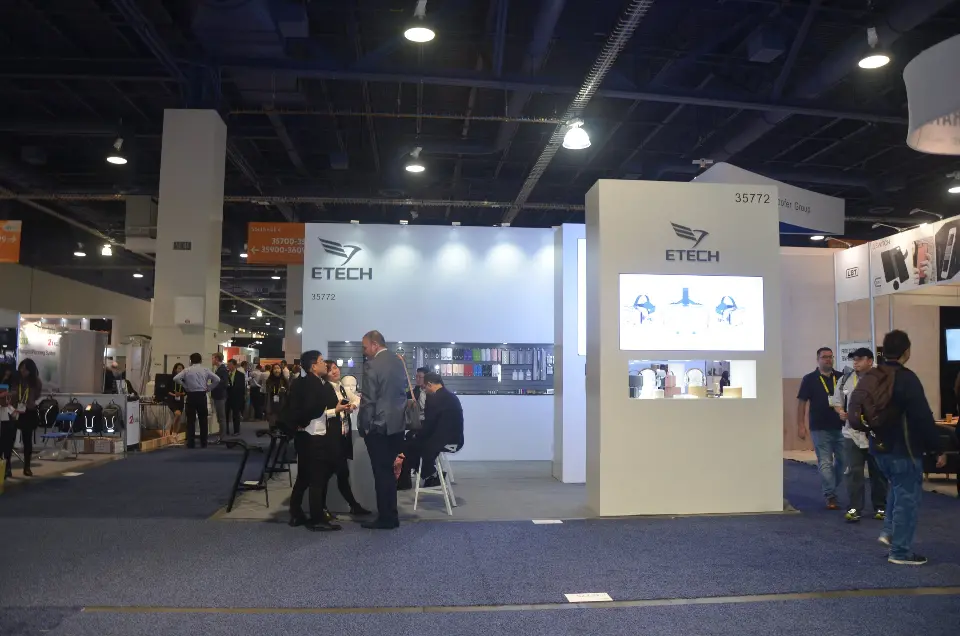 Show-day view of the open booth with guests near the white display wall