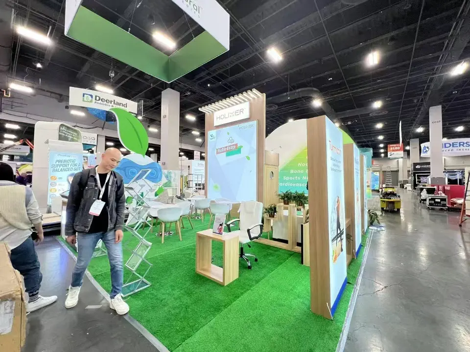 Side view of the green-carpet booth with wood-look framed panels and a visitor walking past