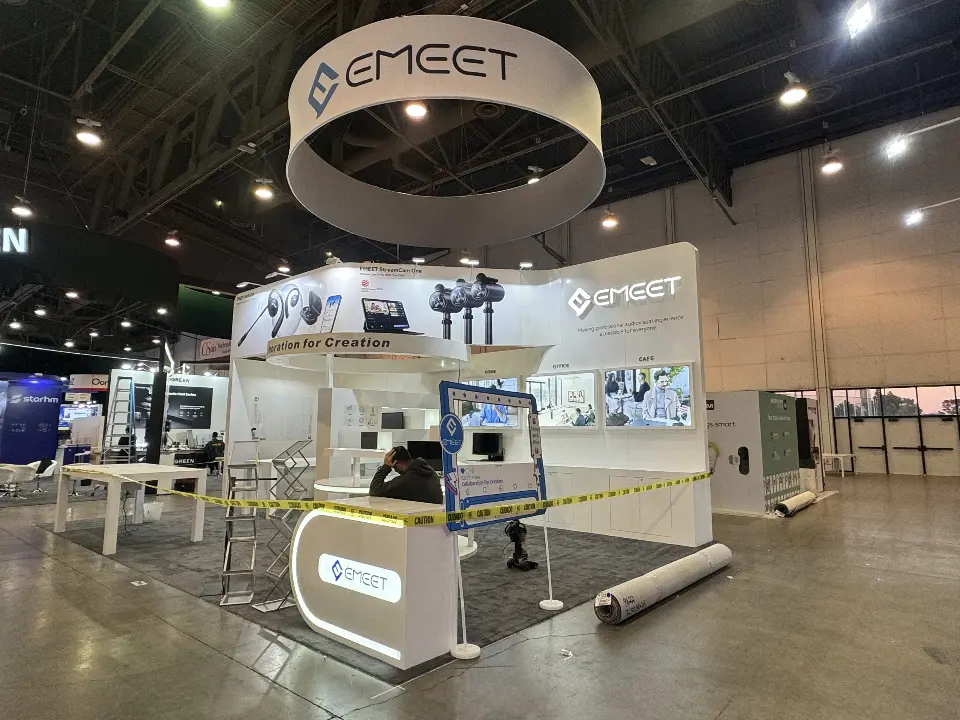 Wide view of the EMEET booth with lit reception counter and hanging ring sign