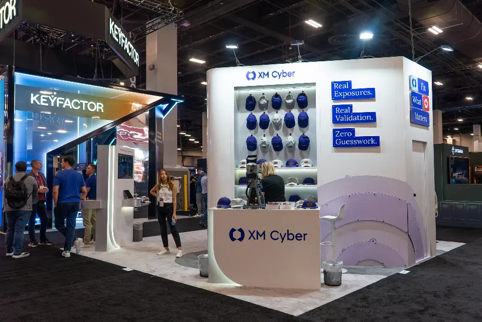 Show-day crowd around the XM Cyber counter and lavender curved wall graphic