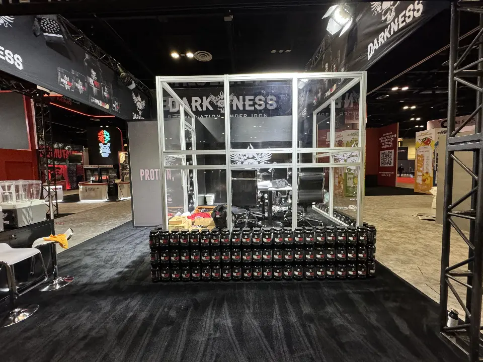 Black DARKNESS booth with cage-style frame, truss uprights and barrel props in front