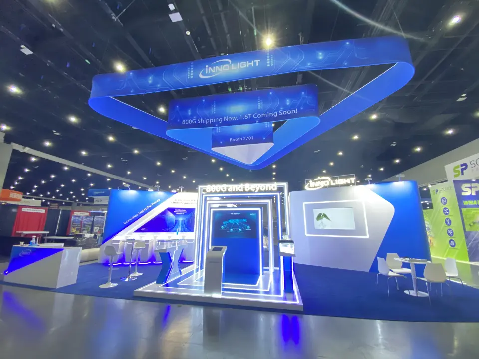 Wide view of the InnoLight booth with blue triangular hanging frame and lit counters