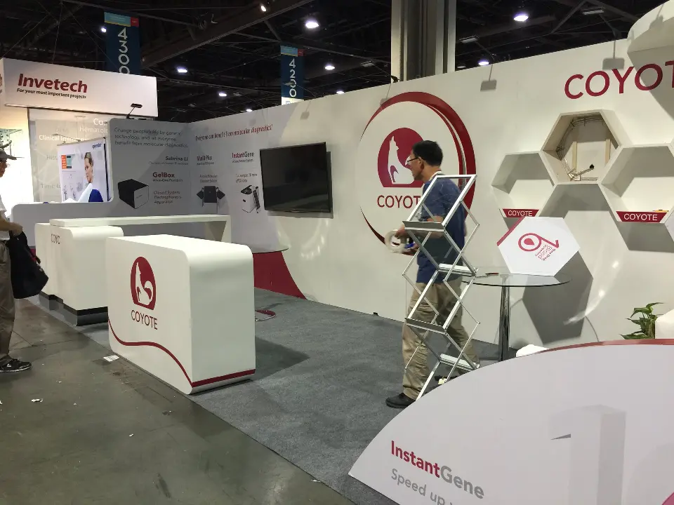 Visitor at the COYOTE counter with a wall-mounted screen and red circular logo behind