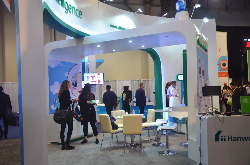 Angled view of the curved white booth with meeting chairs and robot displays