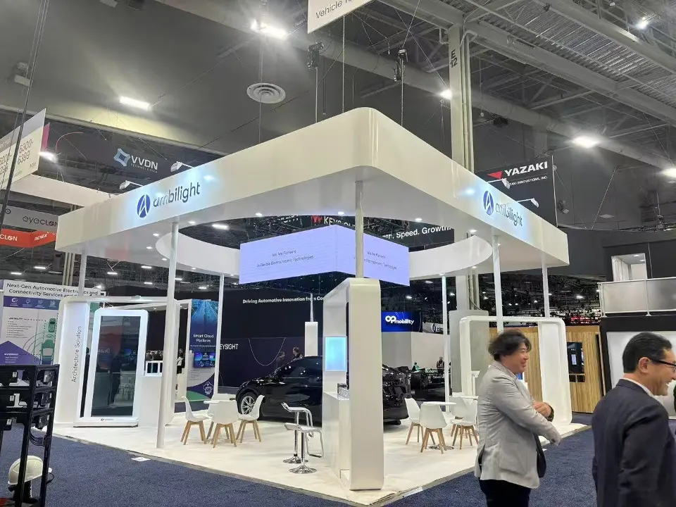 White open Ambilight booth with blue-lit hanging header, display towers and lounge seating