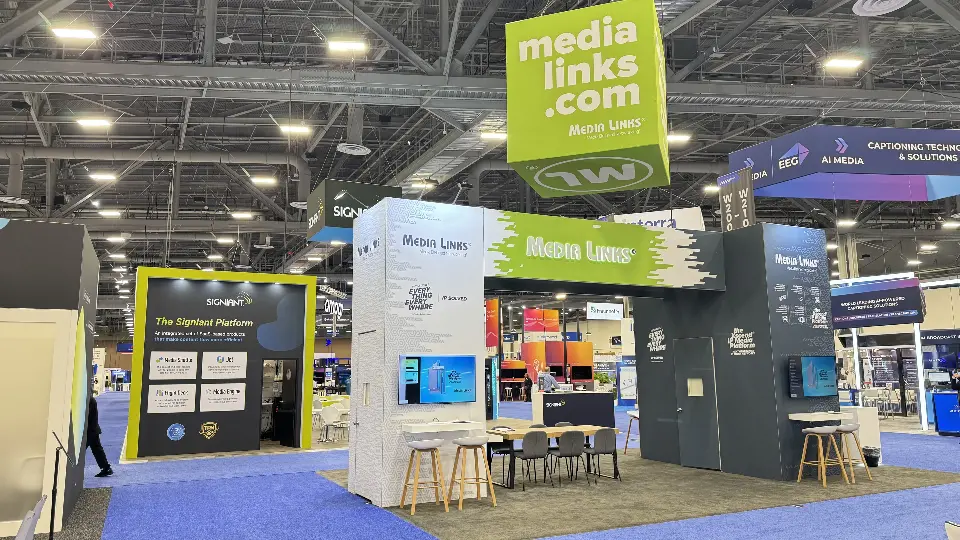 Media Links stand from the aisle with green MEDIA LINKS archway, white and charcoal towers and table