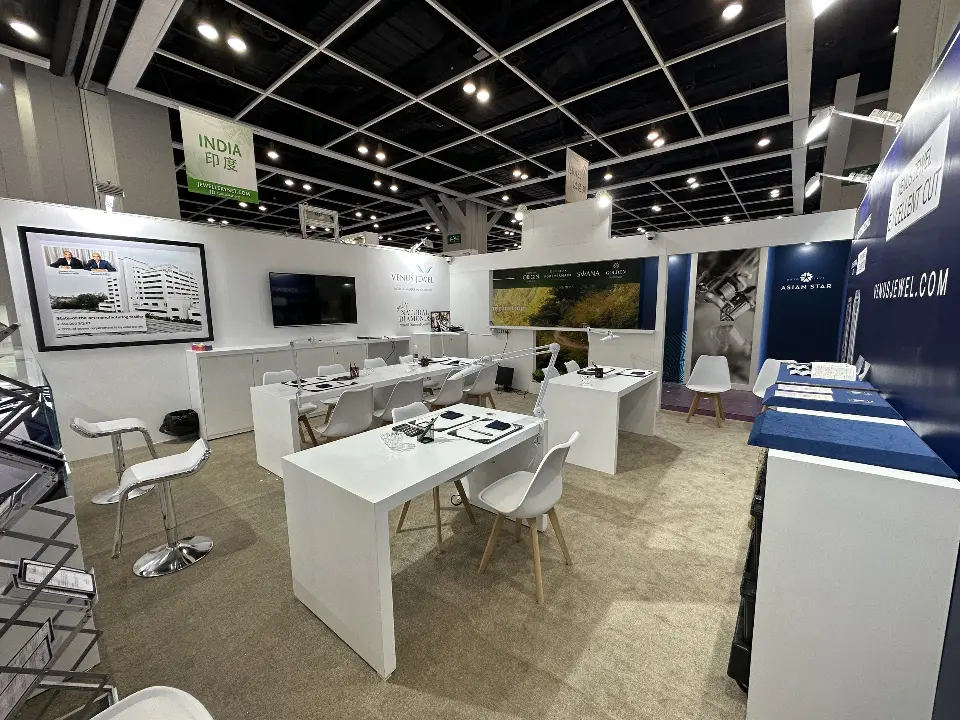 Inside the Venus Jewel booth with white tables, chairs and a wall screen