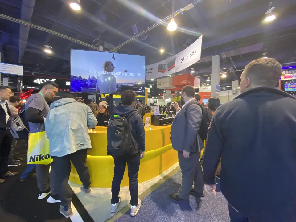 Visitors at the yellow Insta360 counter under a large video screen